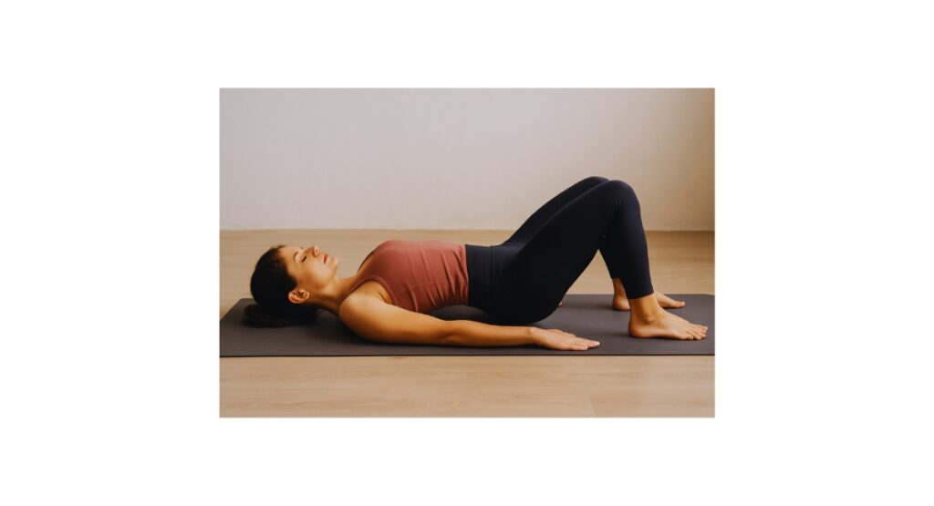 Woman lying on a yoga mat performing pelvic tilts, using slow, mindful movement to release hip tension and support emotional healing through somatic exercise.