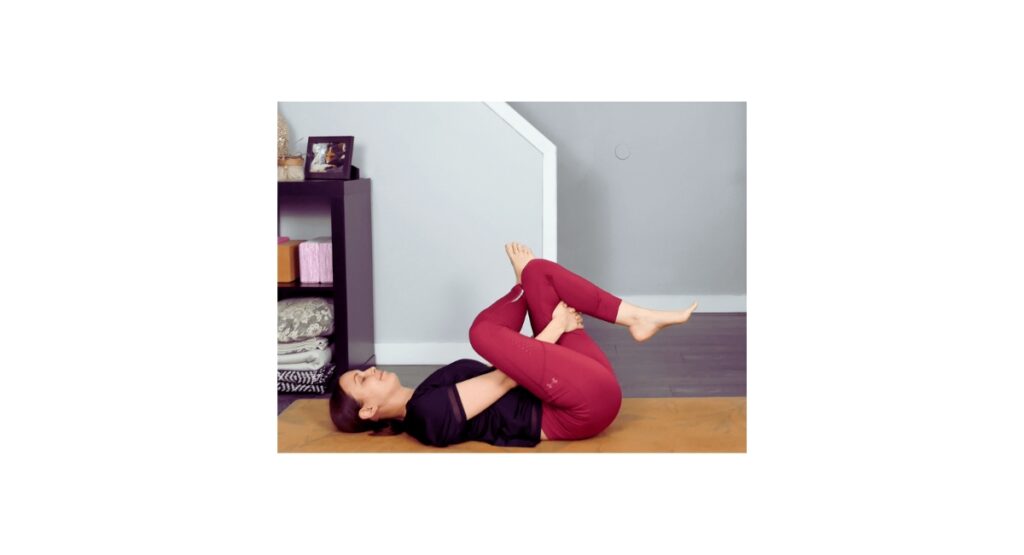 Woman in yoga attire practicing Reclined Pigeon Pose on a mat, gently stretching the hips for somatic hip release and emotional tension relief.